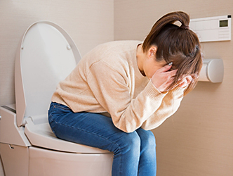 トイレの便座に座って頭を抱えて悩む女性